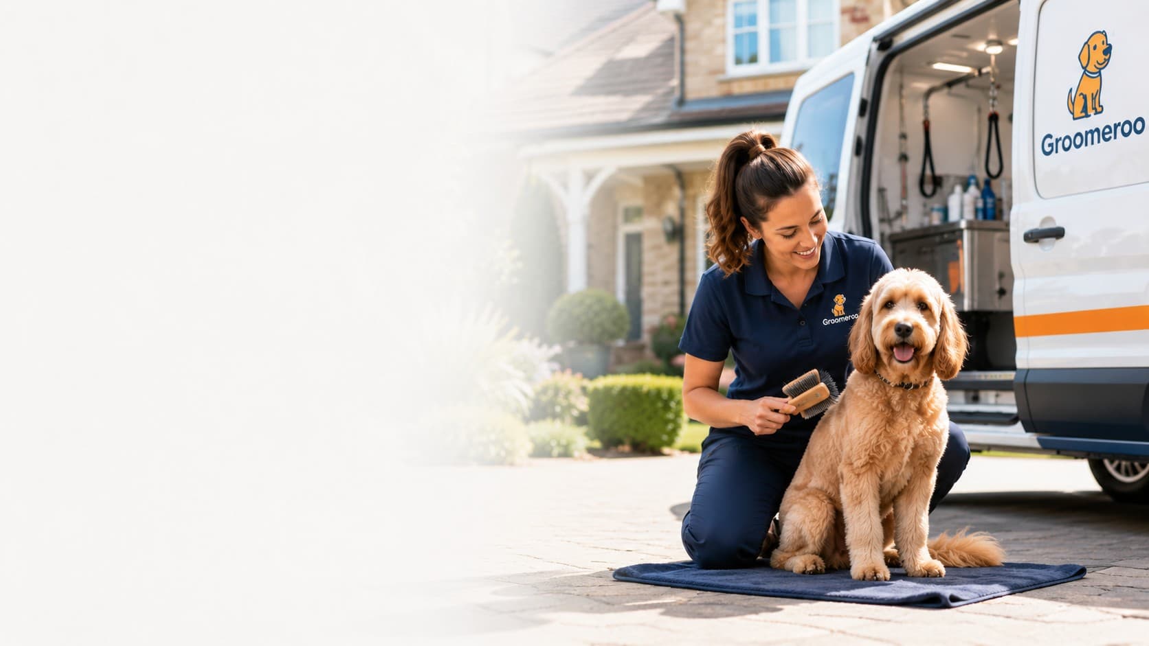 A Groomeroo groomer brushing a happy dog beside the mobile grooming van
